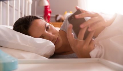 Woman Lying In Bed Checking Messages On Mobile Phone